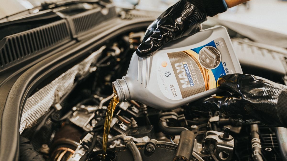 Mecánico con guantes vertiendo aceite nuevo en el motor de un carro