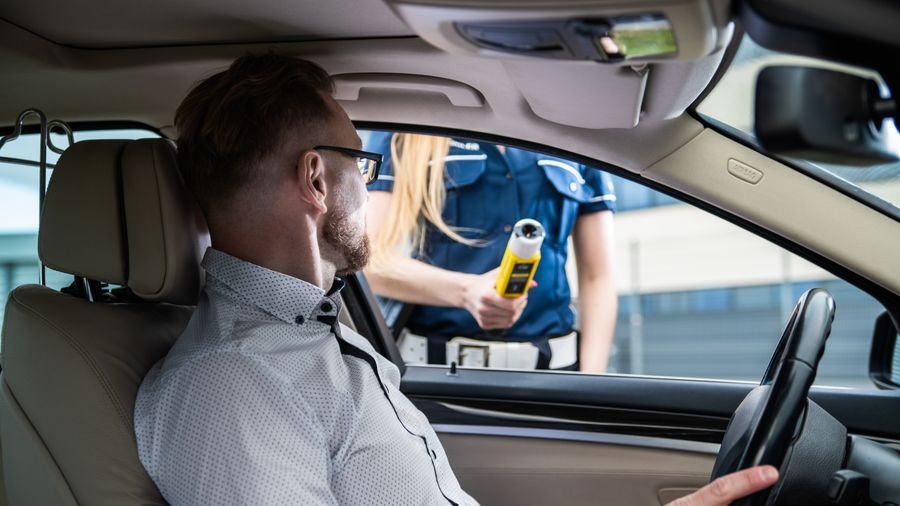 Agente de tránsito acerca un alcohosensor a la ventana de un conductor sentado al volante