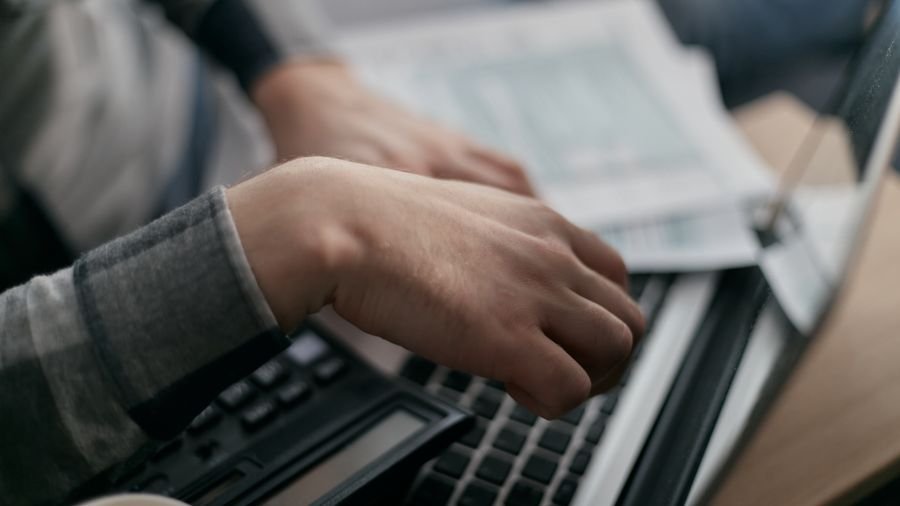 Manos sobre el teclado de un portátil junto a una calculadora y papeles de cuentas