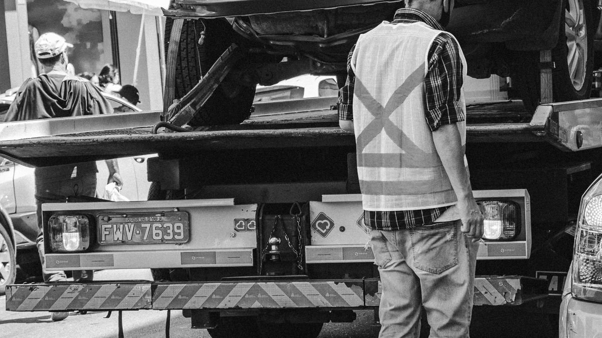 Grúa de plataforma con un carro cargado y un operario con chaleco reflectivo en la calle