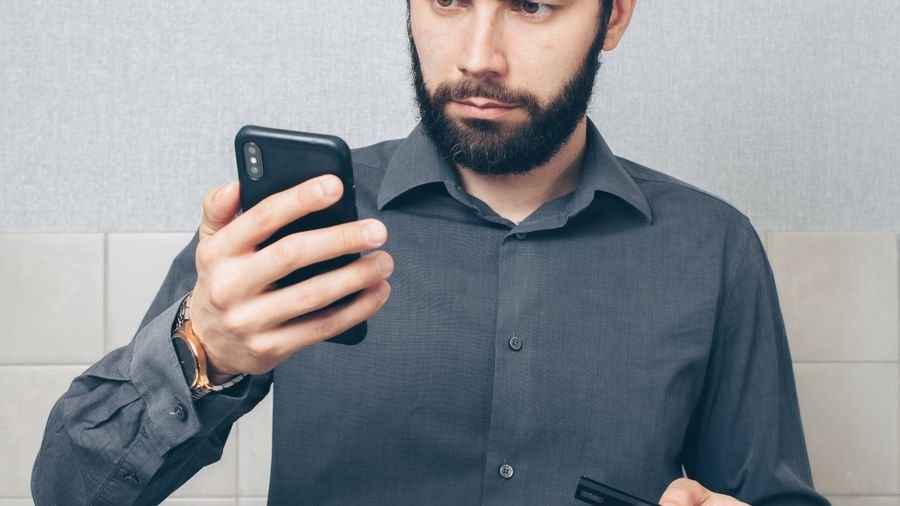 Hombre preocupado revisando su teléfono con cara de mala noticia