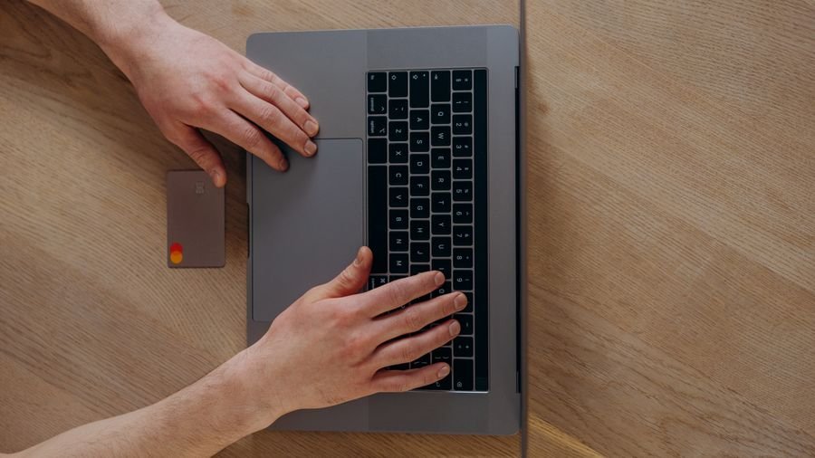 Manos usando un computador portátil con una tarjeta sobre el escritorio