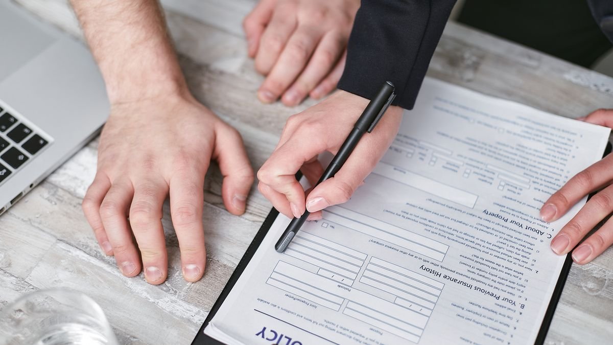 Dos personas firmando un contrato sobre un escritorio de madera