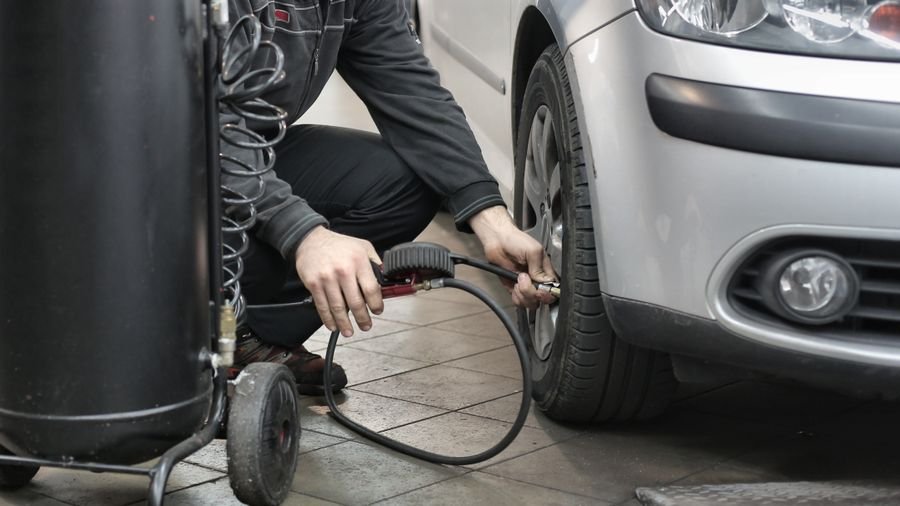 Mecánico agachado inflando la llanta delantera de un carro plateado con una manguera de aire